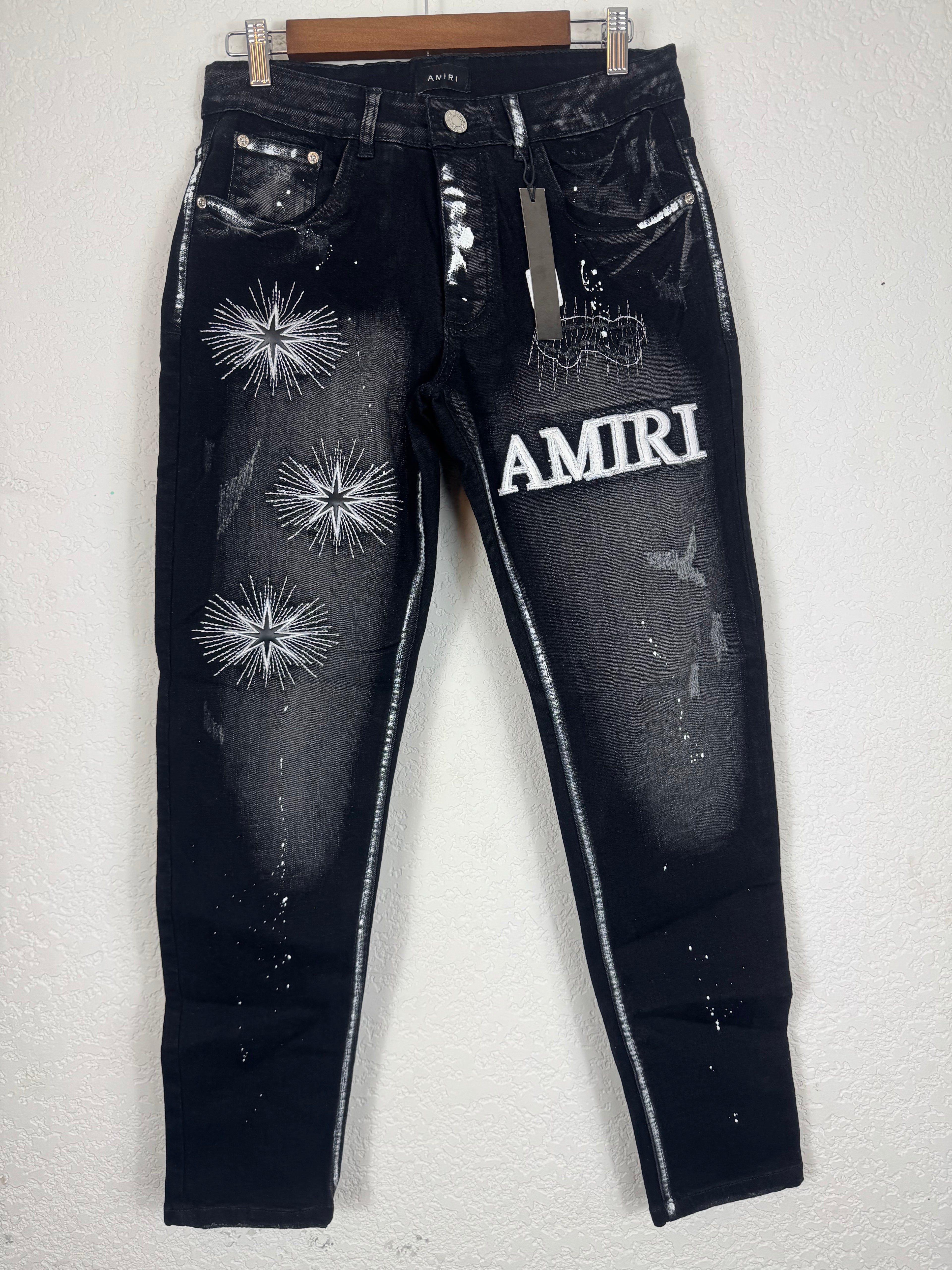 Amiri brand jeans featuring distinctive white starburst embroidery and a prominent logo patc