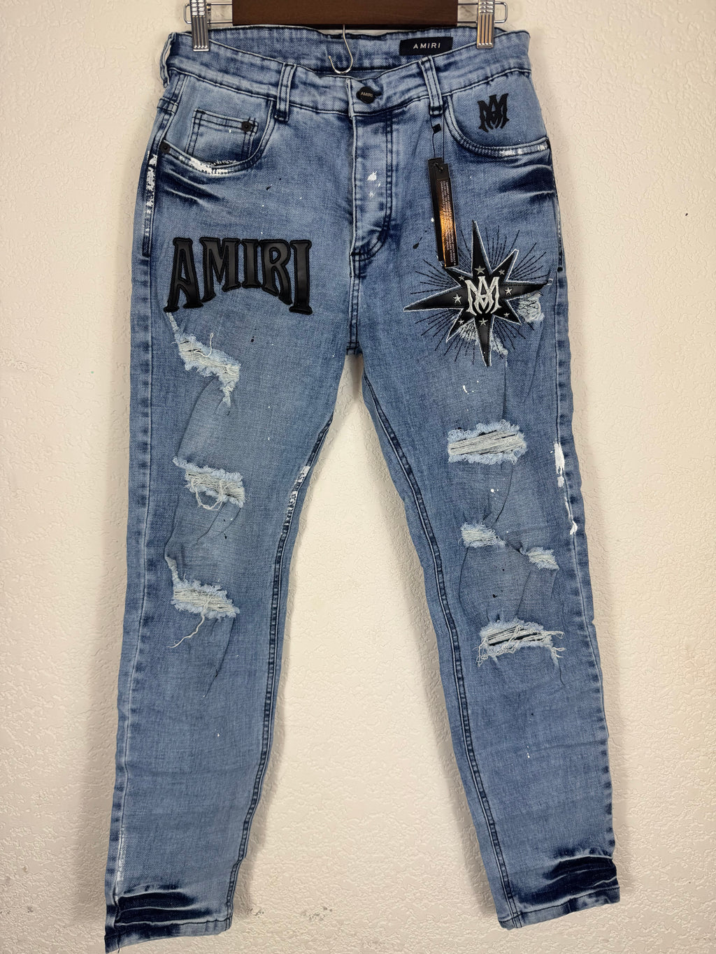 These Amiri distressed blue jeans feature prominent white paint splatters and a large embroidered logo patch.