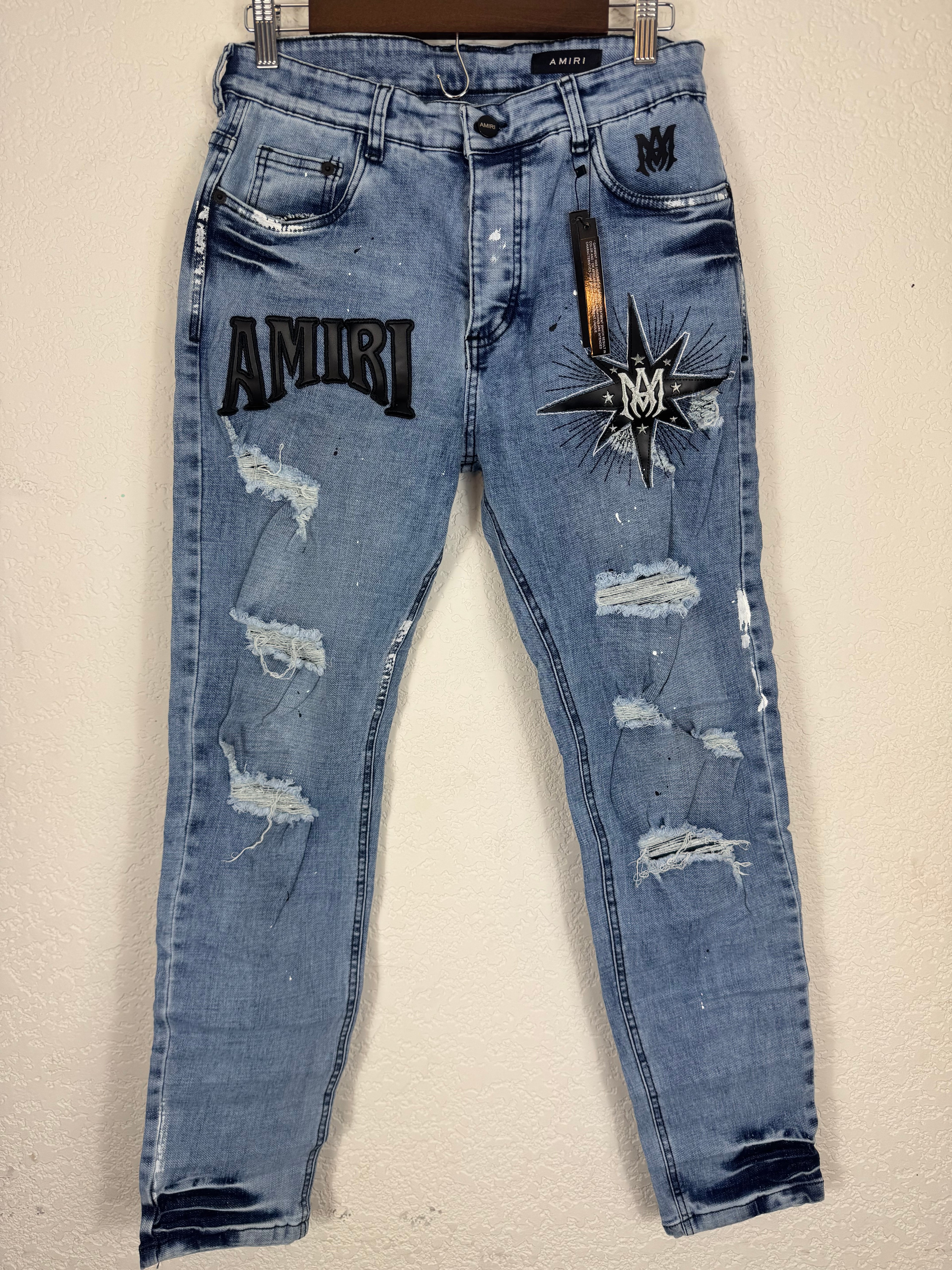 These Amiri distressed blue jeans feature prominent white paint splatters and a large embroidered logo patch.