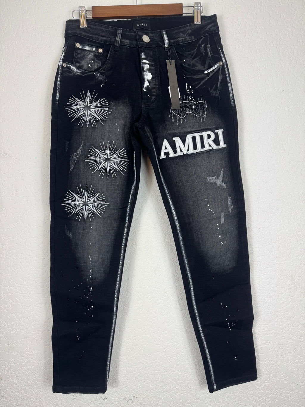 Amiri brand jeans featuring distinctive white starburst embroidery and a prominent logo patc