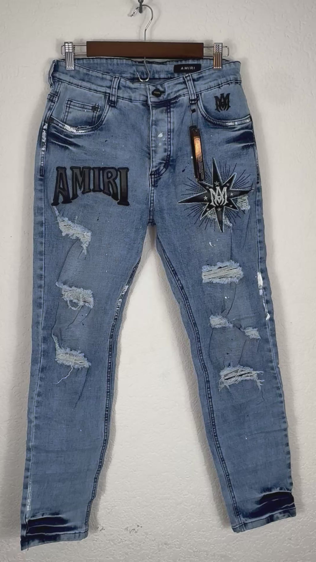 These Amiri distressed blue jeans feature prominent white paint splatters and a large embroidered logo patch.