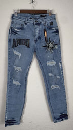 These Amiri distressed blue jeans feature prominent white paint splatters and a large embroidered logo patch.